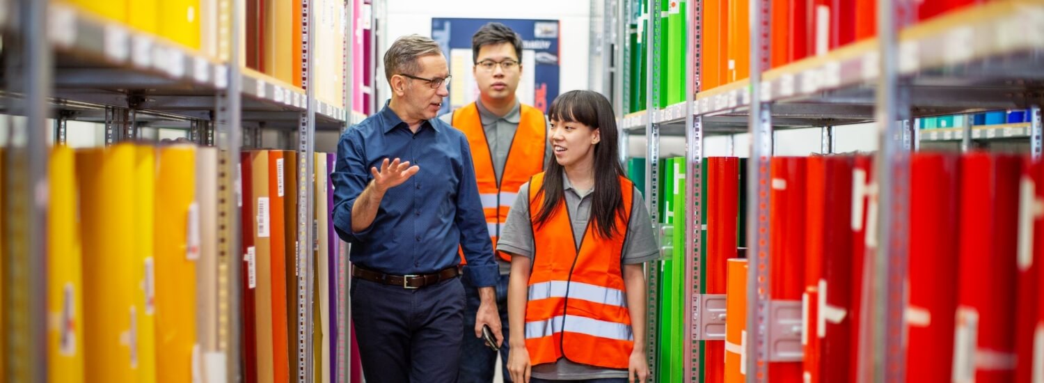 Group of workers walking through storage racks and discussing the stock in warehouse.